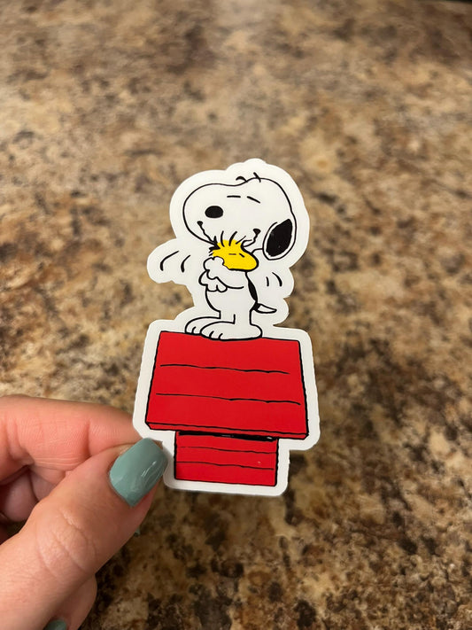 Snoopy and Woodstock Hugging on Red Doghouse – Peanuts Vinyl Sticker for Laptops, Water Bottles, Journals – 3"x1.75" Waterproof Decal